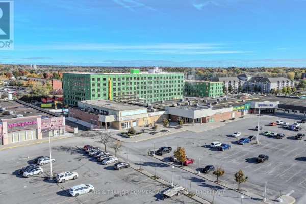 Aerial view of a shopping center with multiple businesses and a parking lot on a sunny day. - D1 - 1300 Bath Road, Kingston