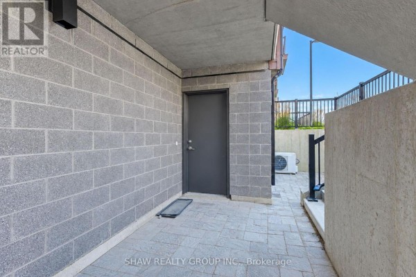 Ground-level patio area with grey block walls, a dark grey door, and stone pavers. - D16 - 10 Palace Street, Kitchener