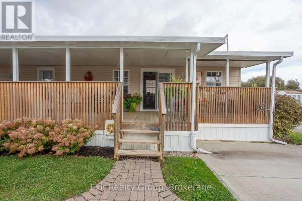 Front entrance to a mobile home with wooden steps leading to a covered deck. - D7 - 153 County Road 27, Prince Edward County