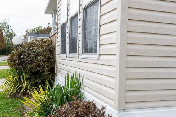 Close-up of the beige vinyl siding and windows on the side of a mobile home. - D7 - 153 County Road 27, Prince Edward County