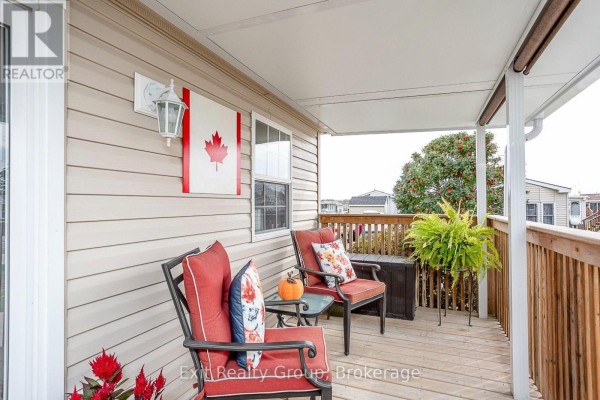 Covered deck of a mobile home with two chairs, a small table, and a Canadian flag. - D7 - 153 County Road 27, Prince Edward County