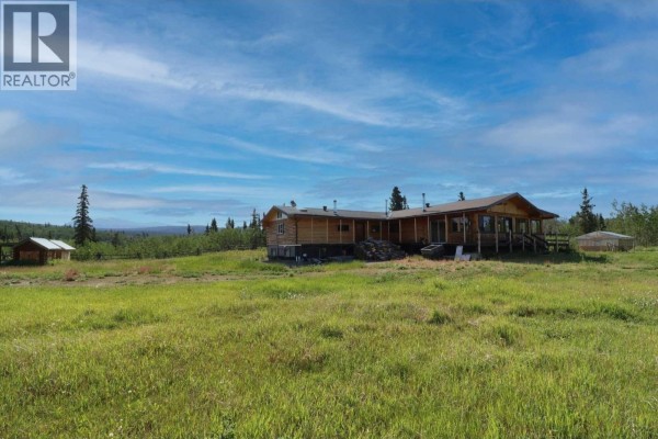 Wide view of the wooden house with a blue sky and distant trees. - Dl 1109 Atlin Road, Atlin
