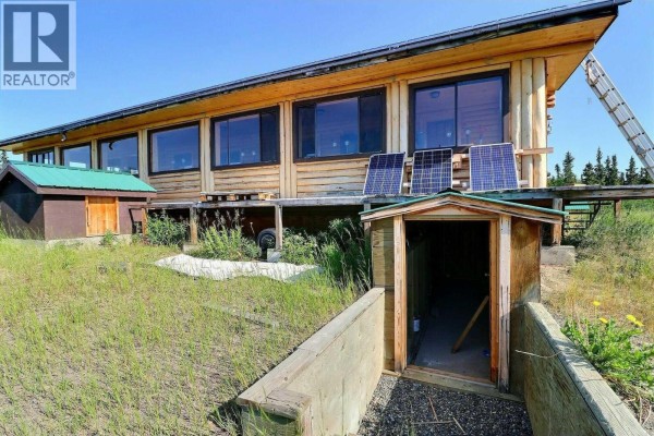 Close-up of the house's foundation with a small storage area and solar panels. - Dl 1109 Atlin Road, Atlin