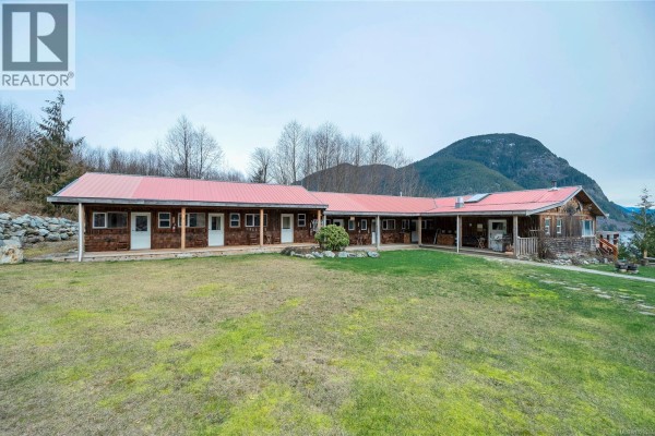 Exterior view of the red-roofed house with landscaped yard and mountains in the background. - Dl1489 Jackson Bay, See Remarks