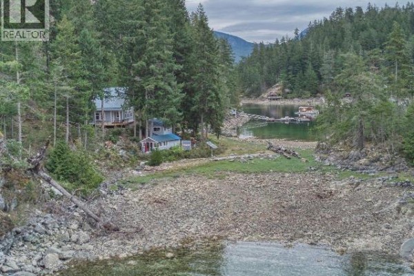 View of houses and cabins nestled on a rocky, tree-lined shore beside a calm body of water. - Dl4946 Refuge Cove, Remote Areas
