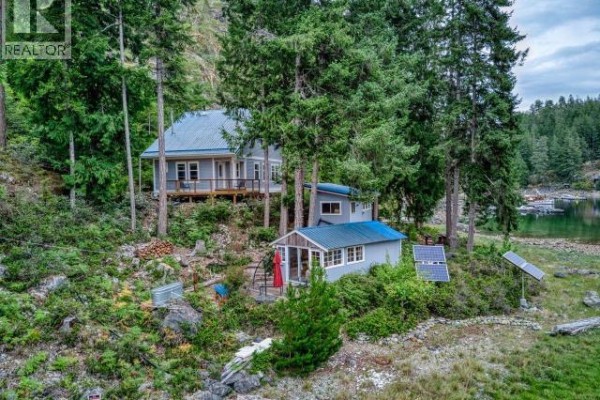 Two grey-sided buildings, a larger house and a smaller cabin, sit on a wooded slope with solar panels. - Dl4946 Refuge Cove, Remote Areas