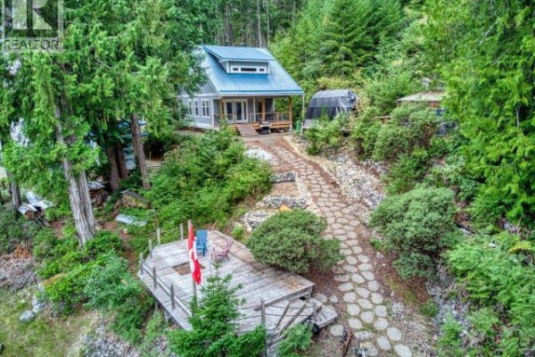 A long wooden dock juts out into the water from a lush green, forested hillside with a grey house. - Dl4946 Refuge Cove, Remote Areas