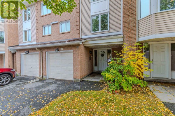 Close-up of townhouse entrance with brickwork, garage door, and green shrubbery. - E - 6 Millrise Lane, Ottawa