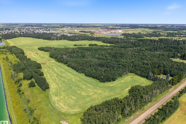 Expansive aerial view of rural land featuring large green fields, dense forests, and a distant town. - E-29-47-24-4 County Of Wetaskiwin, Rural Wetaskiwin County