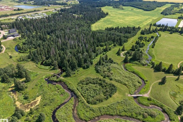 Overhead view of a winding creek with small bridges, surrounded by grassy areas and trees, with houses visible. - E-29-47-24-4 County Of Wetaskiwin, Rural Wetaskiwin County
