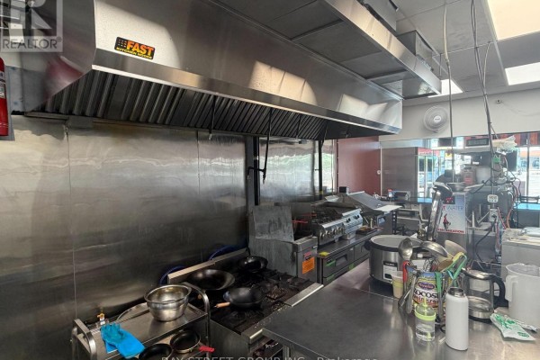 Commercial kitchen with multiple gas stoves, stainless steel surfaces, and an overhead ventilation system. - E107 - 3262 Midland Avenue, Toronto