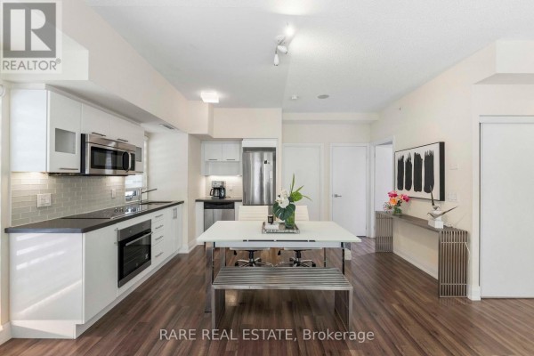 Kitchen with white cabinets, black countertops, stainless steel appliances, and dining area with metal chairs. - E113 - 555 Wilson Avenue, Toronto