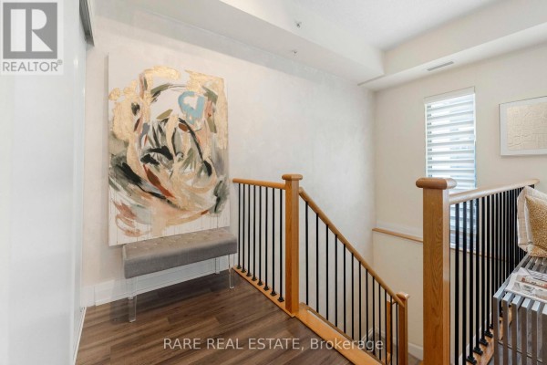 Staircase with wooden handrails and black spindles leading to a landing with abstract art and bench. - E113 - 555 Wilson Avenue, Toronto