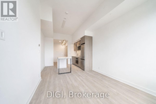 Empty living room with light wood floors, white walls, and view of kitchen. - E438 - 485 Perth Avenue, Toronto