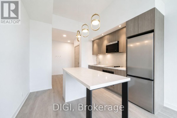 Kitchen island with white quartz countertop and black base, adjacent to light wood cabinets. - E438 - 485 Perth Avenue, Toronto