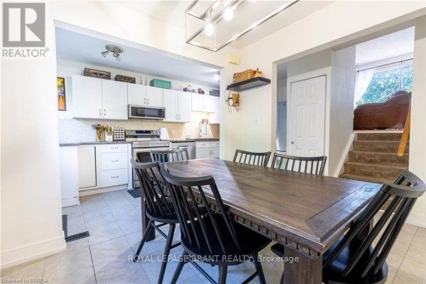 View from dining area shows kitchen and stairs to lower level with upholstered furniture. - E5 - 500 Stone Church Road W, Hamilton