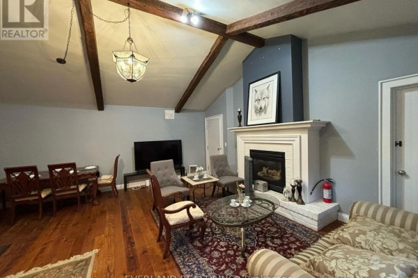 Living room with a fireplace, dining area, and vaulted beamed ceiling. - Ensuite Room - 3369 St Paul Avenue, Niagara Falls