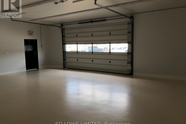 Interior view of empty commercial space with beige floor, white walls, and open roll-up door showing cars. - F1 - 14 Winstar Road, Oro Medonte