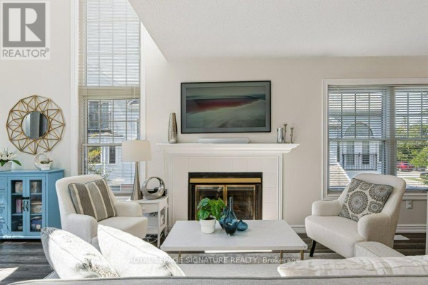 Living room with a white fireplace, two armchairs, a coffee table, and large windows. - F17 - 1667 Nash Road, Clarington