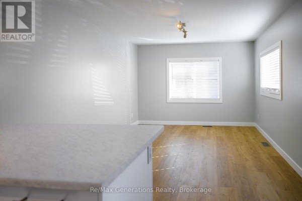 View from a kitchen counter into an empty room with light grey walls and wood laminate flooring. - F3 - 1055 Chippewa Road, Thunder Bay