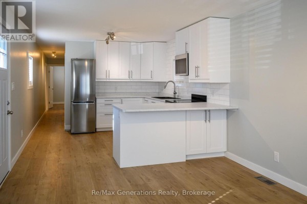 Modern white kitchen with stainless steel appliances, subway tile backsplash, and light wood laminate flooring. - F3 - 1055 Chippewa Road, Thunder Bay