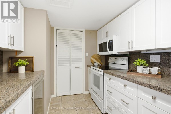 Open kitchen area with white cabinetry, granite countertops, and a breakfast bar. - F304 - 216 Plains Road W, Burlington