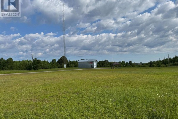 Wide view of a commercial building with a garage door, surrounded by green grass and trees under a cloudy sky. - Fauquier-strickland - 800 Cloutier Road, Kapuskasing