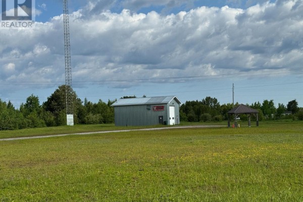 Distant view of the commercial building with a roll-up door and garage, a gazebo, and a tall cell tower. - Fauquier-strickland - 800 Cloutier Road, Kapuskasing