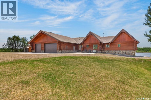 Exterior view of a log home with a stone foundation and a grey garage door. - Flatwater Ranch, Duck Lake Rm No  463