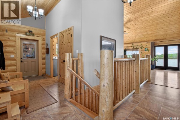 Interior view of a log home entryway with wooden beams, doors, and a staircase railing. - Flatwater Ranch, Duck Lake Rm No  463