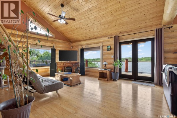 Living room with wood floors, wood-paneled walls and ceiling, and large windows overlooking a lake. - Flatwater Ranch, Duck Lake Rm No  463