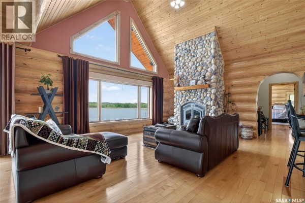Living room with a stone fireplace, leather furniture, and a large window with a lake view. - Flatwater Ranch, Duck Lake Rm No  463