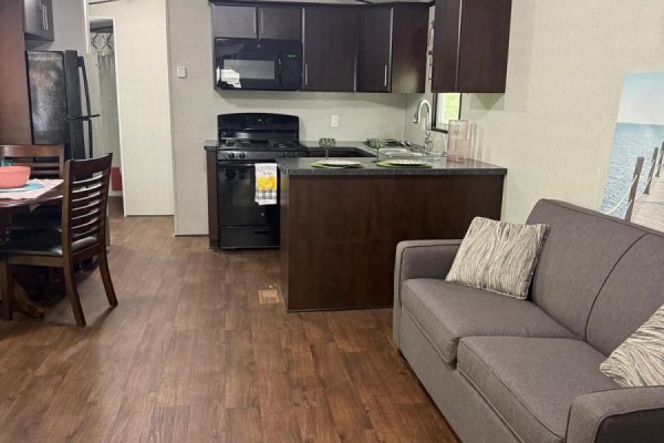 Living room and kitchen area with a grey sofa, dark wood cabinets, and black appliances. - Fnc426 - 1047 Bonnie Lake Camp Road, Bracebridge