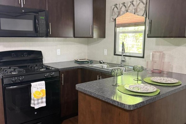 U-shaped kitchen with dark wood cabinets, black countertops, and a small window. - Fnc426 - 1047 Bonnie Lake Camp Road, Bracebridge