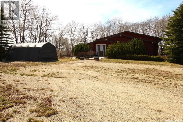 A red house with a dark roof sits on a gravel driveway, beside a large black hoop building. - Frank Acreage, Wawken Rm No  93