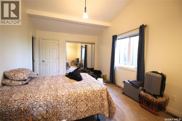 A bedroom with a vaulted ceiling, beige carpet, and a large window with blue curtains. - Frank Acreage, Wawken Rm No  93