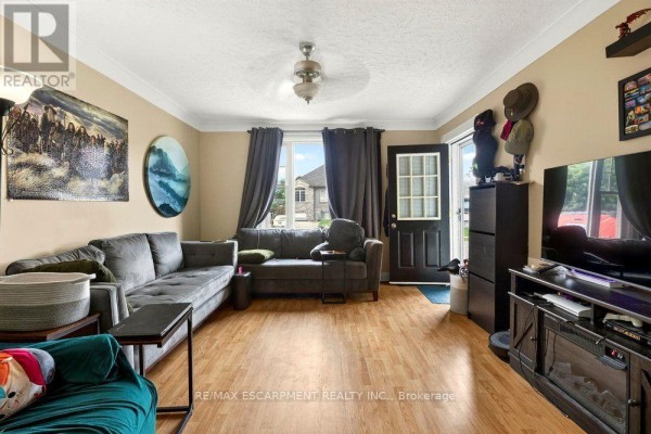 Living room with a sectional sofa, coffee table, television, and door to the outside. - Front - 66 Queen Street S, Thorold