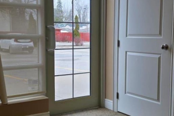 View through glass door and windows to a parking lot with a white car. - G - T4 - 400 Dundas Street, Whitby