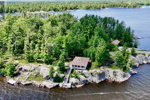 Small wooden cabin with a metal roof and screened-in porch sits on a large granite rock. - G2 West Bay Island, Monetville