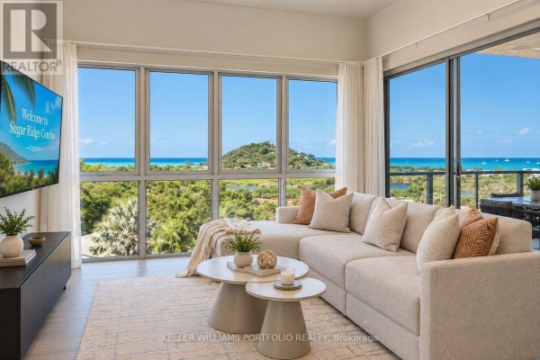Living room with a large sectional sofa, coffee tables, and expansive windows overlooking the ocean and greenery. - Garden Residence - Sugar Ridge Condos Valley Road, Antigua