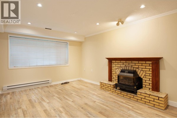 A bright room with a brick fireplace, a large window with blinds, and beige walls. - Ground 4437 Atlee Avenue, Burnaby