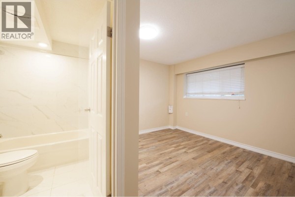 An open doorway reveals a bathroom with a bathtub and toilet, next to an empty beige room. - Ground 4437 Atlee Avenue, Burnaby