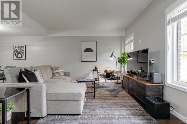 Living room with a grey sectional sofa, dark wood floors, and a large television on a media console. - H - 242 Rachel Crescent, Kitchener