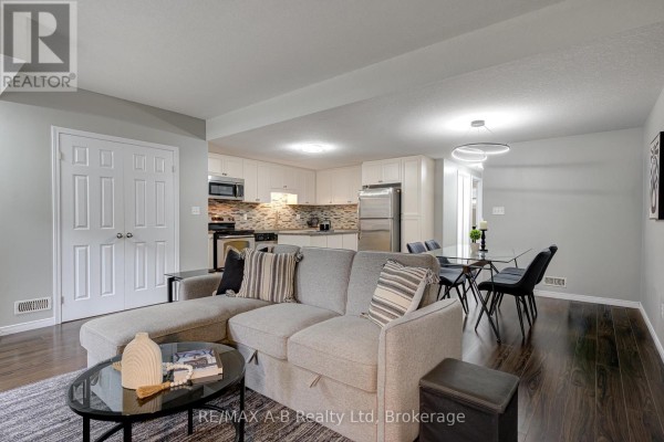 Living and dining area with a sofa, dining table with four chairs, and a white kitchen in the background. - H - 242 Rachel Crescent, Kitchener