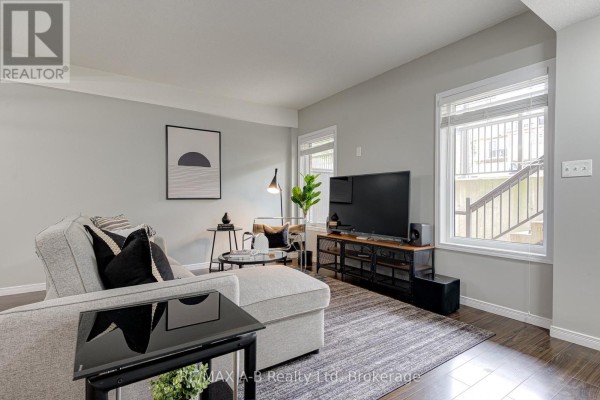 Living room with a large TV, grey sectional sofa, coffee table, and windows overlooking the exterior stairs. - H - 242 Rachel Crescent, Kitchener