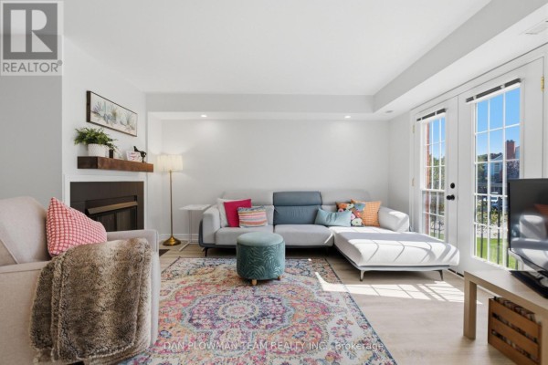 Living room with sectional sofa, armchair, TV, and double doors leading outside. - H11 - 76 - 1661 Nash Road, Clarington
