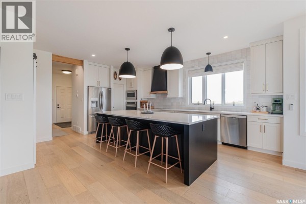 Kitchen island with black stools, white countertops, stainless steel appliances, and white cabinetry. - Hayter Acreage, Dufferin Rm No  190