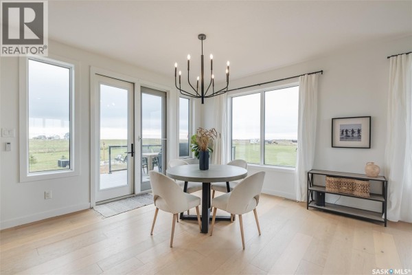 Dining area with a round table, upholstered chairs, and large windows overlooking a grassy field. - Hayter Acreage, Dufferin Rm No  190