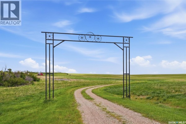 A dirt driveway leads through a metal archway with decorative wheels towards the property. - Highway 15 Outlook Acreage, Rudy Rm No  284
