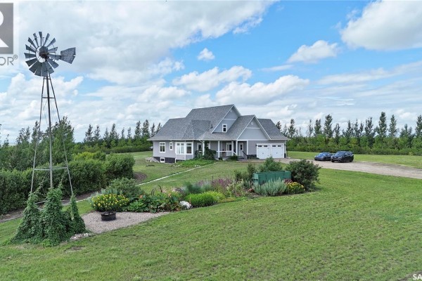 A light grey house with a grey roof and a front porch is seen with a windmill. - Highway 15 Outlook Acreage, Rudy Rm No  284